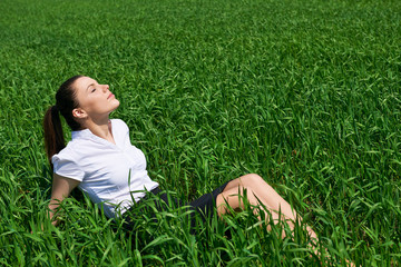 Business woman relaxing in green grass field outdoor under sun. Beautiful young girl dressed in suit resting, spring landscape, bright sunny day