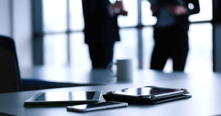 tablet, mobile cell phone and cup of coffee  in office with business people in backgorund