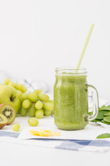 Green smoothie in glass jar made of apples, celery, grapes, spinach and kiwi on white cloth background. Healthy drink concept