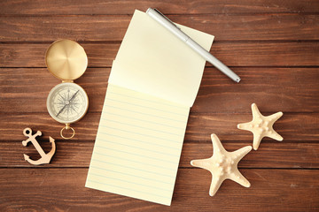 Open notepad, pen, compass and travel decorations on wooden background