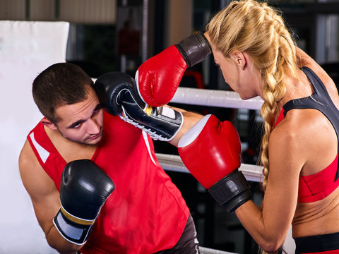 Boxing workout woman in fitness class ring. Sport box exercise two people. Man trainer holding sport mitts in gym. Female box gloves are red backview.