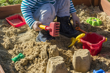 Child playing with plastic rakes on sandbox.