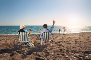 Portrait of a happy family in summer nature. Mother and father are sitting on a beach deck chair,...