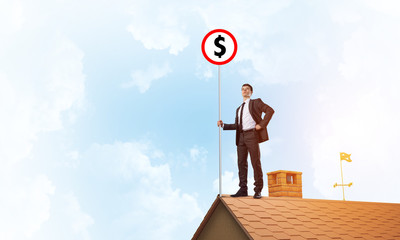 Businessman on house roof showing roadsign with money concept. Mixed media