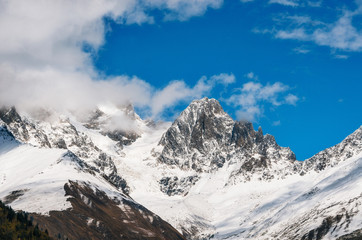 Obraz premium Snow covered mountains and their peaks in the clouds against the blue sky in Georgia. Greater Caucasus Mountains