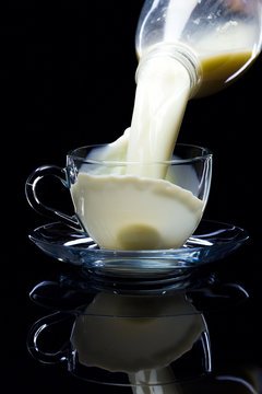 Natural milk is poured into clean glassware, black background, studio light