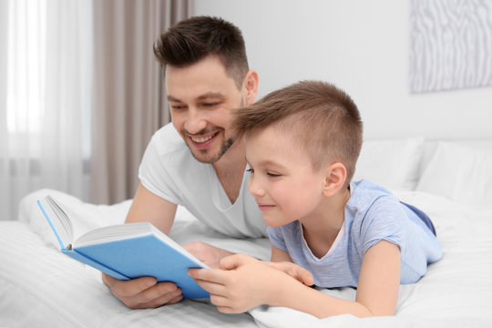 Dad and son reading interesting book while lying on bed at home