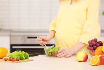 Young pregnant woman eating salad in kitchen