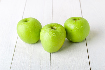 Three wet green apples on white wooden background. Close up.
