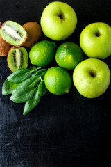 Ingredients for smoothie. Green fruits on black wooden background. Apple, lime, spinach, kiwi. Detox. Healthy food. Top view. Copy space.