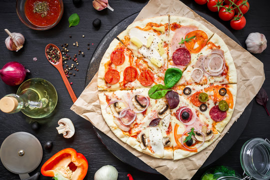 Tasty italian pizza with ingredients, spices, oil and vegetables on dark background. Flat lay, top view.