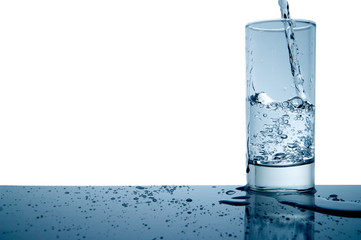 water splashing in a glass and on the table with copyspace, isolated and blue toned.