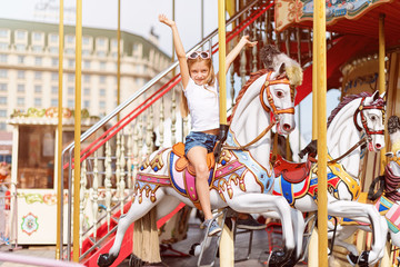 Fototapeta na wymiar Girl riding on a merry go round. Little girl playing on carousel, summer fun, happy childhood and vacation concept