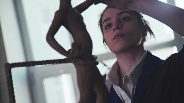 Good young woman makes a sculpture on light art studio with big window. She is concentrated and molds a woman. The human statue from clay. Craftsman artist making craft, pottery.