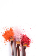 Makeup brushes with blush or eyeshadow of pink, red and coral tones sprinkled on white background