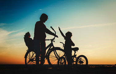Obraz na płótnie Canvas father with two kids on bikes at sunset beach