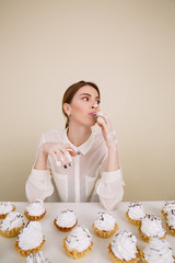 Concentrated young lady posing while eating cupcakes.