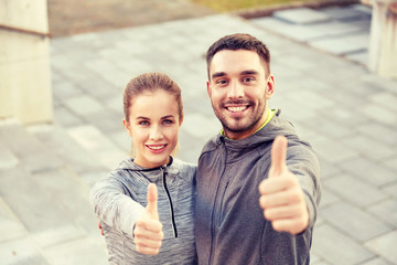 smiling couple showing thumbs up on city street