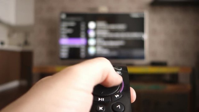 Male hand holding the TV remote control and turn off smart tv. Channel surfing, focused on the hand and remote control. Internet TV. Programm on demand.