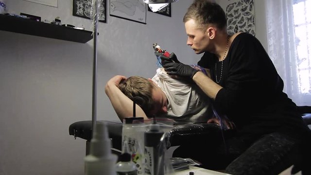 The tattoo artist makes a black tattoo on man shoulder