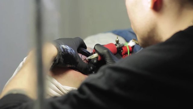 The tattoo artist makes a black tattoo on man shoulder