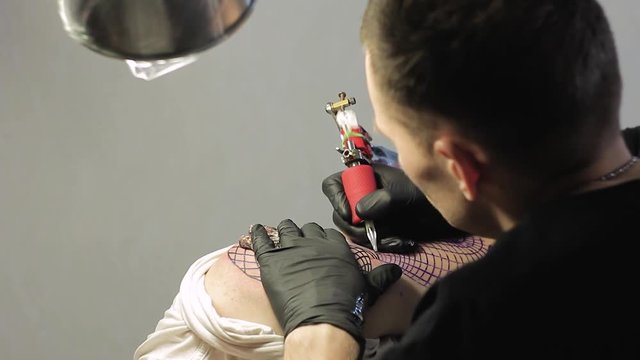 The tattoo artist makes a black tattoo on man shoulder