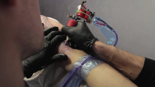 The tattoo artist makes a black tattoo on man shoulder
