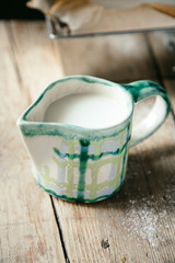 Handcrafted creamer in checkerboard pattern with nilk on wooden background with copy space. Rustic concept.