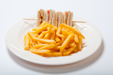 Club sandwiches with chicken and french fries on a white plate