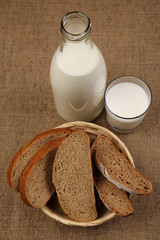 Milk and bread. Milk in a glass bottle and rye bread on a sackcloth background. Bio products for the breakfast. Healthy food. Top view.