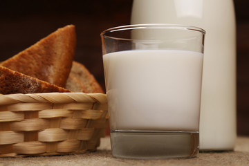 Milk and bread. Milk in a glass bottle and rye bread on a dark background. Bio products for the breakfast. Healthy food. Close up.