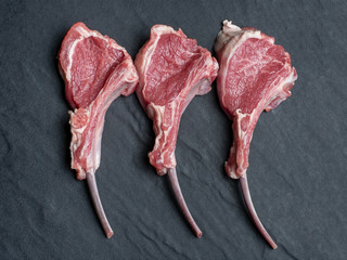 three raw lamb chops on a black slate plate from above