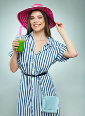 Smiling woman wearing striped dress and summer hat drinking green detox smoothie