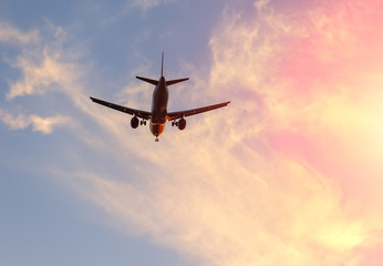 Modern Airplane in sky at sunrise among pink clouds