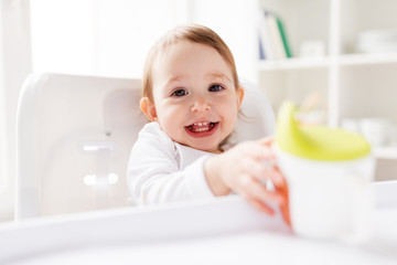 baby drinking from spout cup in highchair at home