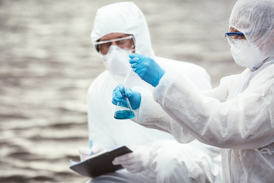 Ecologysts wearing protective uniforms examining the liquid contents of a test tube.