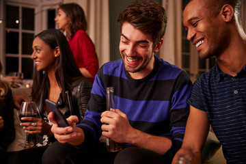 Man Looking At Message On Mobile Phone At Party