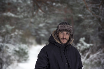 Fototapeta na wymiar Young man in warm clothing and hat walking in winter forest