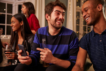 Man Looking At Message On Mobile Phone At Party