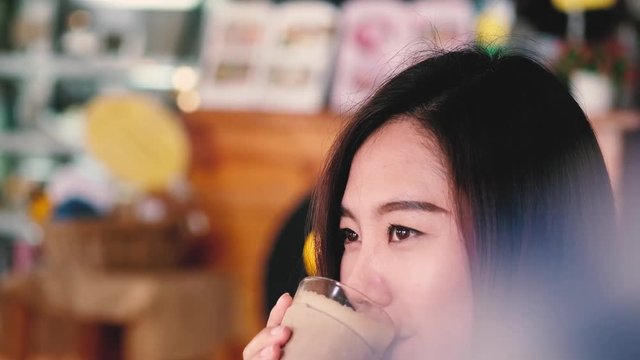 A beautiful Asian girl with smiley face holding and drinking coffee in modern cafe