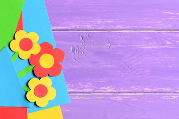 Colourful paper flowers, paper sheets on purple wooden background with copy empty space for text. Bright flowers card. Summer or spring backdrop