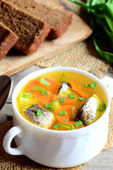 Diet, simple and tasty fish soup. Home fish soup with potatoes, carrots and green onions in a bowl. Rye bread pieces, fresh green onion on vintage wooden table. Closeup. Vertical photo