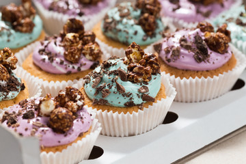 Vanilla cupcakes with blue and purple cream, chocolate and popcorn in delivery box, selective focus, close up