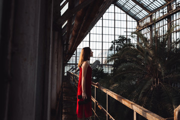 Woman in red dress standing and holding binoculars at greenhouse