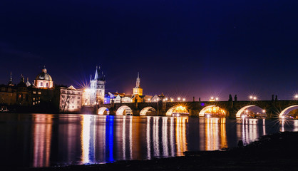 Fototapeta na wymiar Charles bridge in Prague at night with lights reflected in water of Vltava