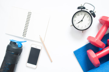 Flat lay of smartphone with sport yoga equipments and clock on white background