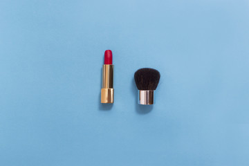 Top view of makeup set: red lipstick and makeup brush on pastel background.