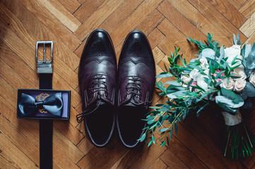 Close up of modern man accessories. Black bowtie, leather shoes, belt and wedding bouquet on wood rustic background. Set for formal style of wearing