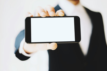 Businessman in a black suit showing smartphone with horizontal blank white display.Clean mockup, blurred background.