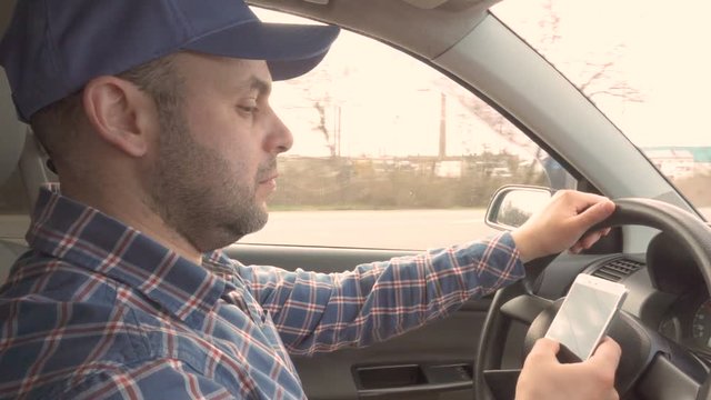 Man uses a smartphone while driving.  Men texts while driving.